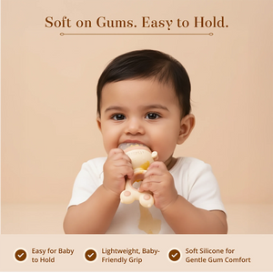 A baby is shown holding and biting a Laalan Paalan Baby Fruit Pacifier against a warm beige background with marketing text "soft on gums. Easy to hold" 