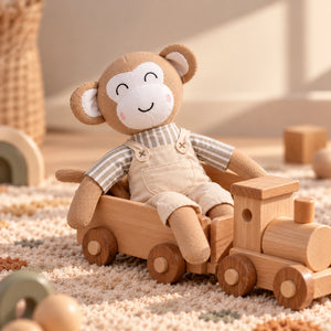 A plush soft monkey toy wearing beige overalls and a striped shirt, sitting in a wooden train on a textured rug in a softly lit nursery setting.