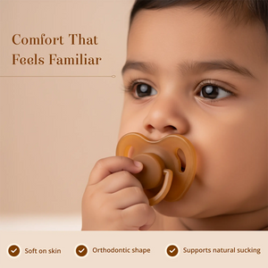 A close-up of a baby holding a Sneh Dulaar Baby Pacifier to their mouth, with text reading 'Comfort That Feels Familiar' and feature callouts at the bottom.