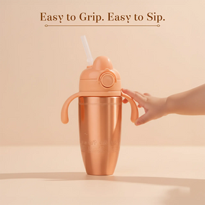 A child's Tiny Tamba Pure Copper Sipper  with a metallic rose gold finish, featuring a matching handle, straw lid, and a hand reaching to turn a side valve. 