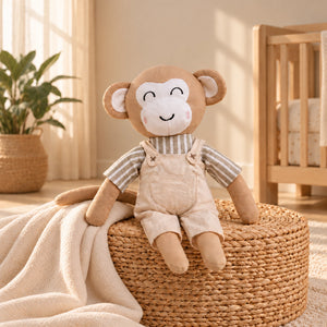 A plush monkey toy with a smiling face, wearing beige overalls and a striped shirt, sitting on a woven round ottoman in a softly lit nursery setting.