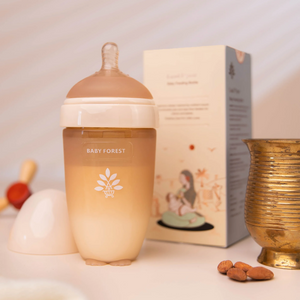 A Baby Forest silicone baby feeding bottle with a frosted amber body and white collar, shown alongside its product packaging box and a small gold decorative cup on a light tabletop.