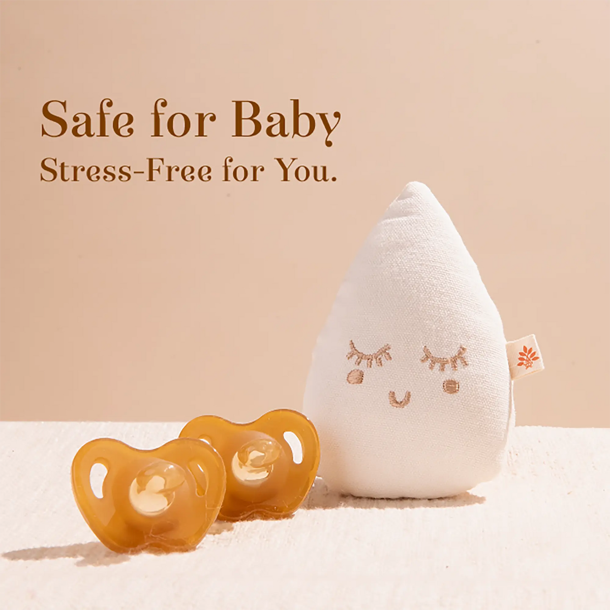 Two amber-colored Sneh Dulaar Baby Pacifier and a white teardrop-shaped plush baby pillow.