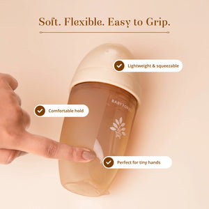 A Laad Pyaar Baby Feeding Bottle with a translucent amber body and a cream-colored cap, shown with a hand holding it.