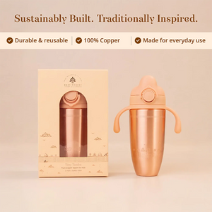 A Tiny Tamba Pure Copper Sipper for Kids with a matching handle lid stands beside its cream-colored product box on a warm beige background. 