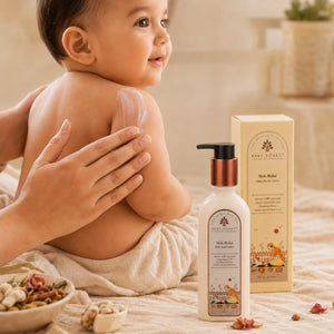 A baby sits on a cream-colored blanket while an adult applies Moh Malai Baby Body Lotion to the baby's back.