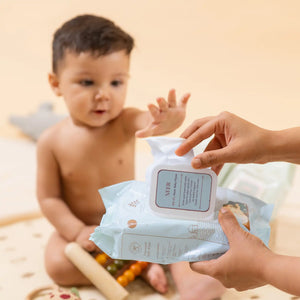 Baby reaching out towards a package of Neer 99.9% Water Baby Wipes with a blurred background