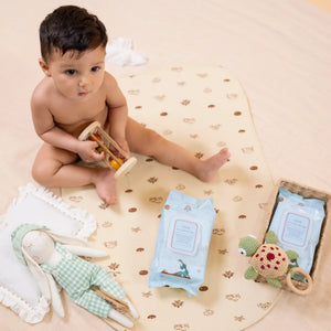 Baby playing with toys on a patterned mat with wet wipes and a plush toy.