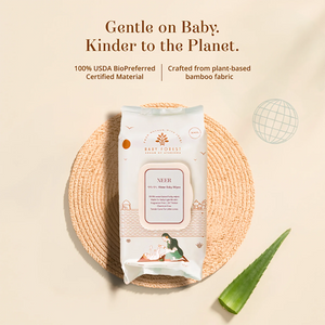 A package of Baby Essentials Neer 100% BioPreferred baby wet wipes sits on a woven round mat, with a green aloe vera leaf beside it on a warm beige background. Text above reads 'Gentle on Baby. Kinder to the Planet.'